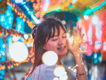 Portrait of young woman against illuminated blurred lights at night