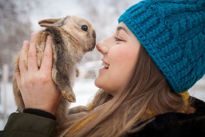 Close-up of cheerful woman holding rabbit while standing on field during winter