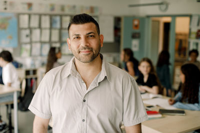 Portrait of smiling male tutor standing in classroom