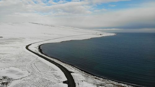 Empty road next to snowed mountain and blue water icelandic fjord