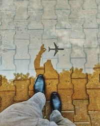 Low section of man standing by airplane reflection on footpath