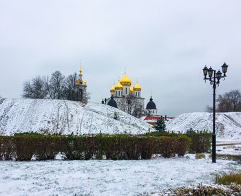 Traditional windmill by building against sky during winter