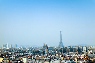 Eiffel tower amidst buildings against clear blue sky on sunny day in city