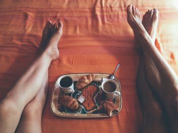 Low section of naked man and woman relaxing by food tray on bed