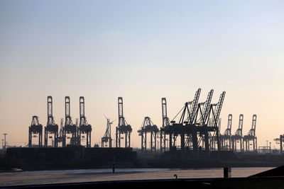 Cranes at harbor against clear sky