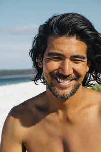 Close-up of happy shirtless man looking down while sitting at hyams beach against sky during sunny day