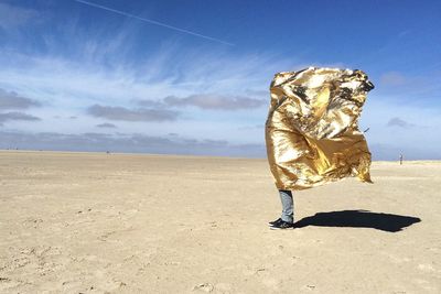 Man on desert protecting from heat being covered with golden foil 