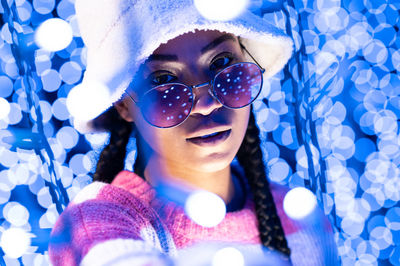 Joyful woman of color with a white beanie braided hairstyle and pink glasses enjoying the christmas