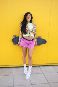 Portrait of smiling young woman standing against yellow wall