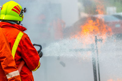 Rear view of firefighter spraying water on fire while standing at street