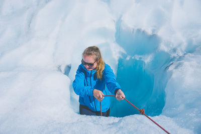High angle view of young woman pulling rope while standing amidst snow
