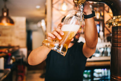 Cropped image of woman holding beer glass at bar
