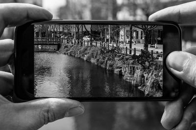 Cropped hands of person photographing river with mobile phone