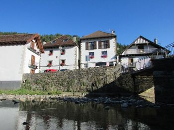 Houses by river and buildings against clear sky