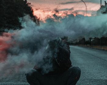 Man sitting behind smoke on road during sunset