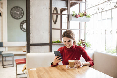 Young woman using phone while sitting on table