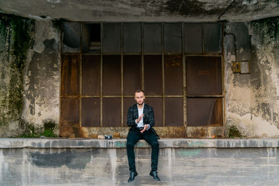 Young man sitting against old building