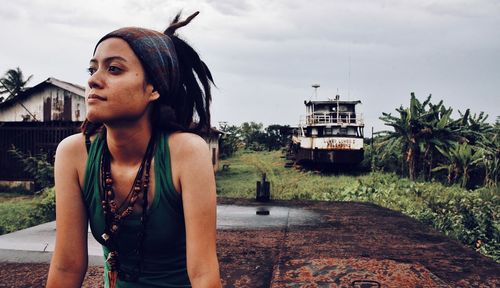 Young dreadlock woman looking away while standing against sky