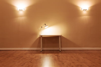 Illuminated lamp on floor against wall