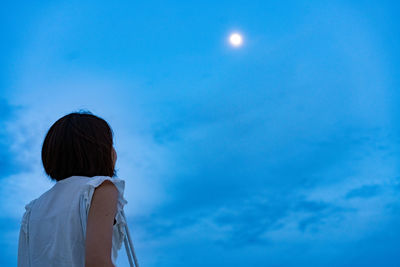 Low angle view of woman looking at moon in blue sky