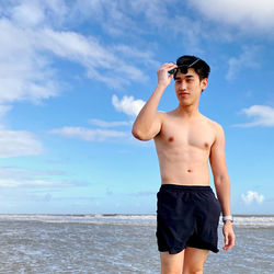 Full length of shirtless man standing at beach against sky