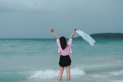 Rear view of woman with arms raised standing in sea against sky