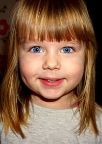 Close-up portrait of cute smiling girl with bangs and blue eyes at home