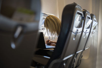 Female entrepreneur working on laptop and write notes sitting near window in an airplane