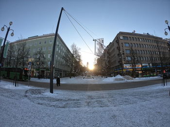 Snow covered road by buildings against sky