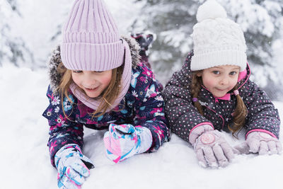 Siblings lying on snow during winter