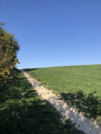 Road amidst field against clear sky