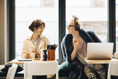 Smiling customers talking while sitting against window in coffee shop