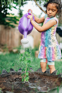 Diverse mixed race pre school girl outdoors during summer watering plants in garden