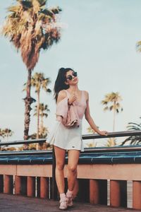 Full length portrait of young woman standing by railing against sky