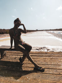 Woman sitting on wood at beach against sky