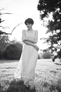 Portrait of beautiful young woman wearing evening gown while standing on field against sky