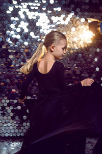 Girl in a black dress dancing in the studio on a background with sequins