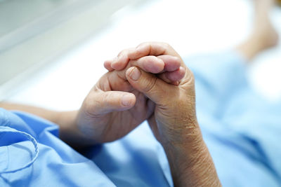 Low section of female patient holding hands while sitting on hospital bed