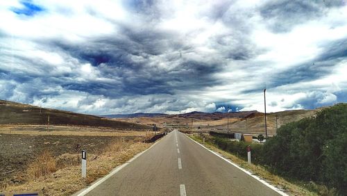 Surface level of country road along landscape against cloudy sky