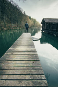 Rear view of man standing on pier over lake against sky