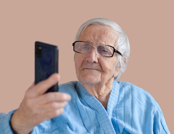 Portrait of elderly 90 years woman wearing glasses and blue jacket holding camera and taking selfie.