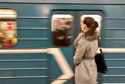 Blurred motion of train by mid adult woman standing at railroad station