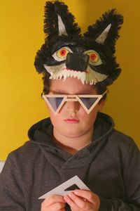 Portrait of boy holding carnival mask against yellow background