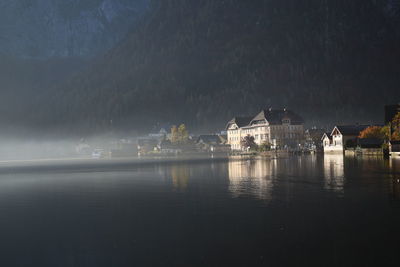 Illuminated buildings by lake against sky at night