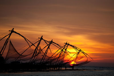 Silhouette fishing nets on sea against sky during sunset