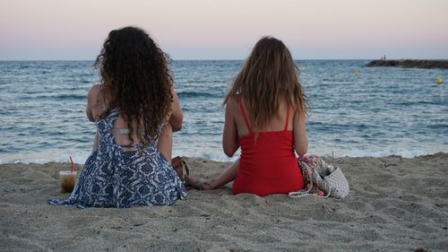 Rear view of women sitting on shore at beach against sky