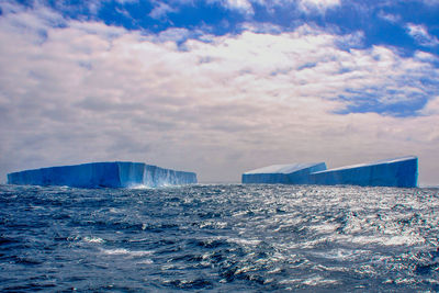 Icebergs in sea against cloudy sky during sunset