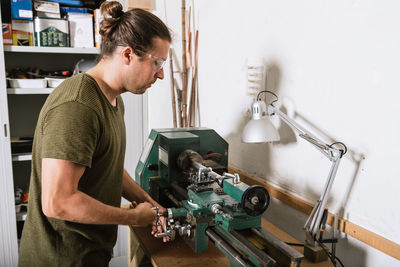 Handsome male woodworker standing at workbench and measuring detail with caliper tool while working in workshop