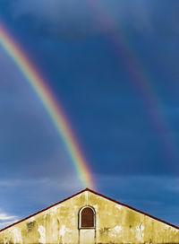 Low angle view of rainbow over building against sky