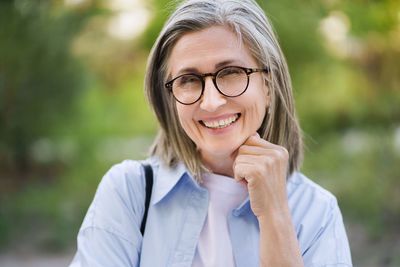 Happy mature woman with silver hair and glasses smiling outdoors